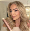 vrouw met blond golvend haar houdt airstyler met roségouden krulstuk vast