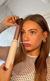 vrouw houdt roségouden airstyler bij blond haar, tekst the process